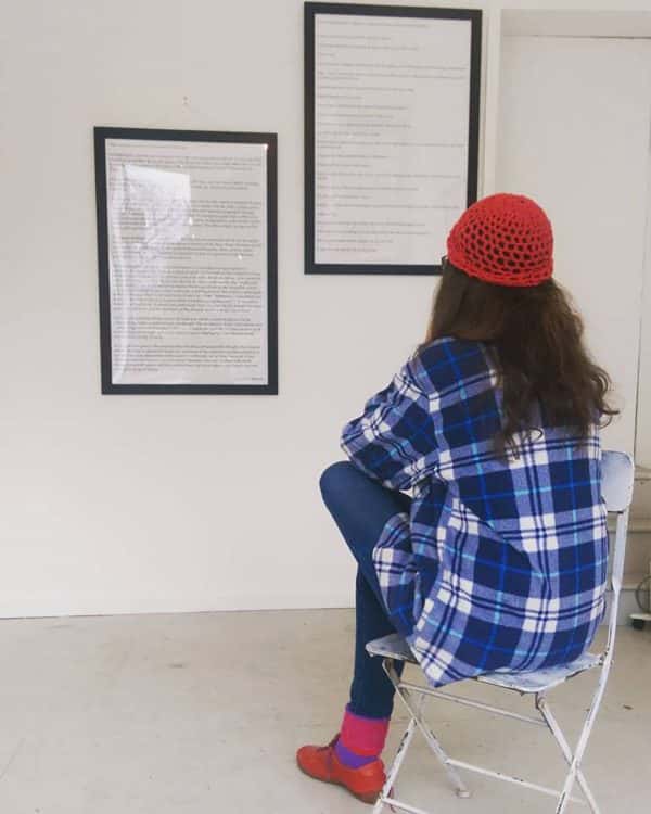 Jade Anderson - Person sitting in a folding chair to read two framed documents mounted on the wall