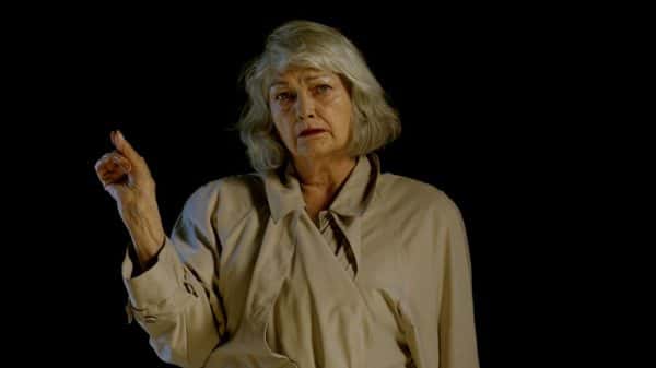 Leo Baldwin-Ramult - A woman with medium length grey hair and a beige raincoat pointing a finger