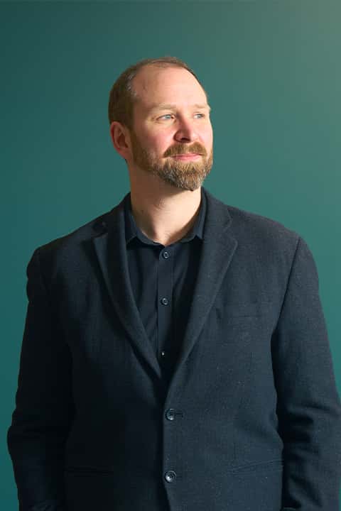 Staff portrait image of Mark Wickham, ‪Director of Computer Arts and Technology at Norwich University of the Arts‬. Mark wears a buttoned up shirt under a suit jacket