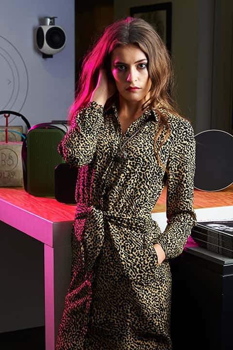 Fashion Excess Shoot, Norwich Fasion Week Publication - Photograph of a woman with long brown hair in a leopard print dress with bright pink lighting from the left