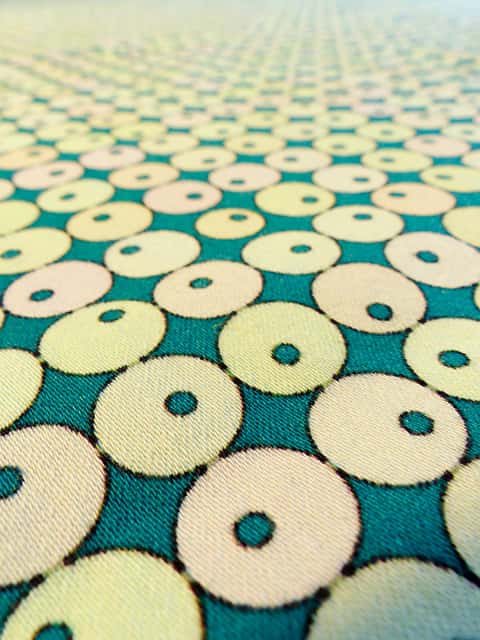 Spot the Difference (detail) - Close up of a fabric surface in a mid green colour, covered in pale yellow circles in rows with smaller green circles inside