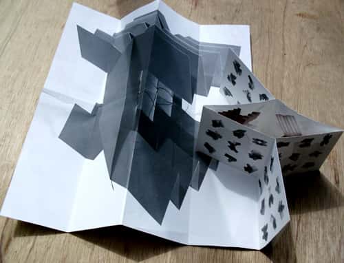 Bookmare- Design for printed matter - Aerial view of a concertina book that has folded out, with a black geometric design on white paper