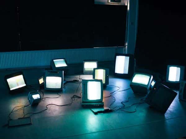 Neil James Earl, MA Moving Image and Sound - Image of several vintage televisions sets arranged on a floor in a dark studio space, the light from the screen creates shadows on the floor, created by MA Moving Image and Sound student Neil James Earl
