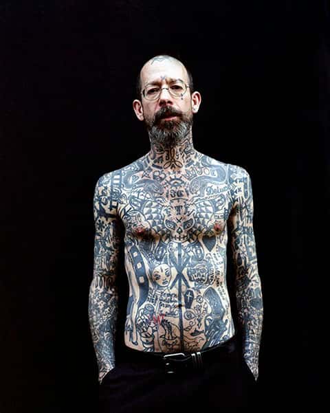 Duncan - Photograph with a black background of a bare-torsoed man covered in tattoos by Ross Trevail