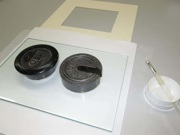  - Weights on a sheet of thick glass over the back of a white card to flatten it into a frame