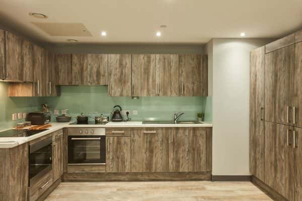 Crown Place kitchen - NUA Crown Place kitchen area with wooden cabinets and floor, and glass splashback