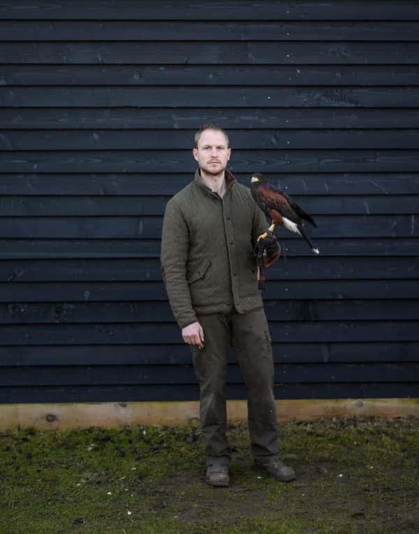 Benjamin Leech - Man standing with a bird of prey on his arm standing next to a blue wall, photo by BA Photography student Benjamin Leach