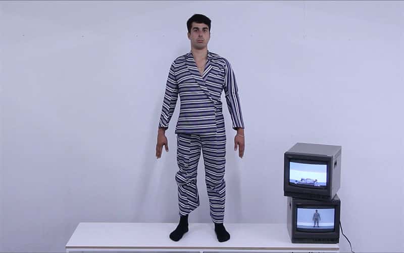Photo of a young man in a white and black striped outfit, stood on a white plinth