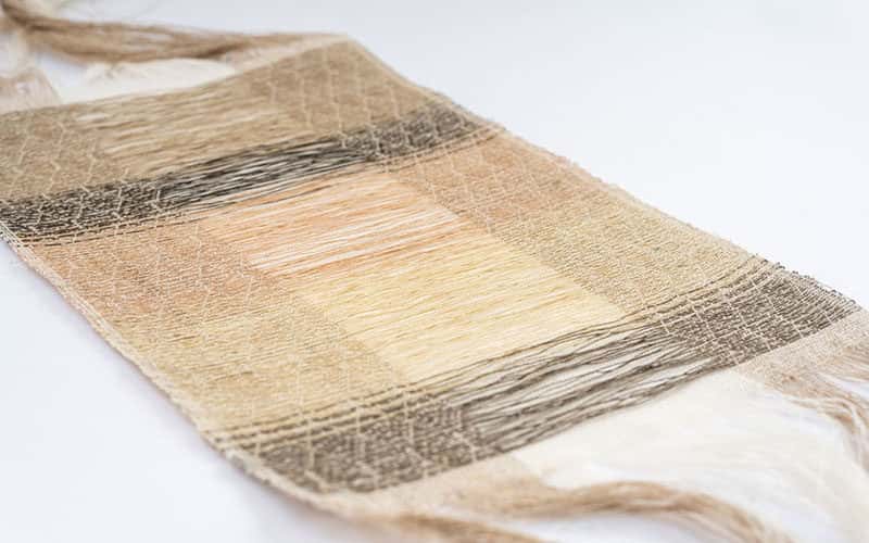 Delicate woven strip of textiles in pale colours laid flat on a white surface