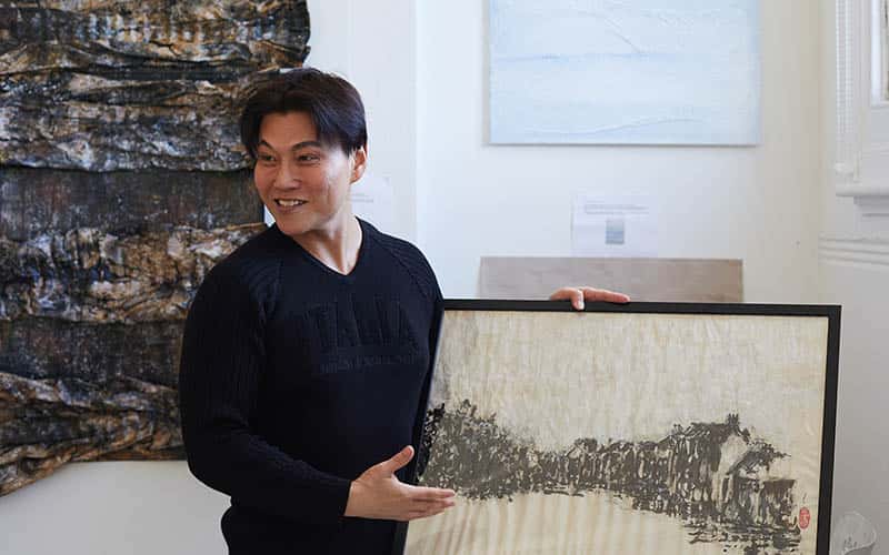 Photo of a man in a black top holding a black and white drawing and looking away from the camera