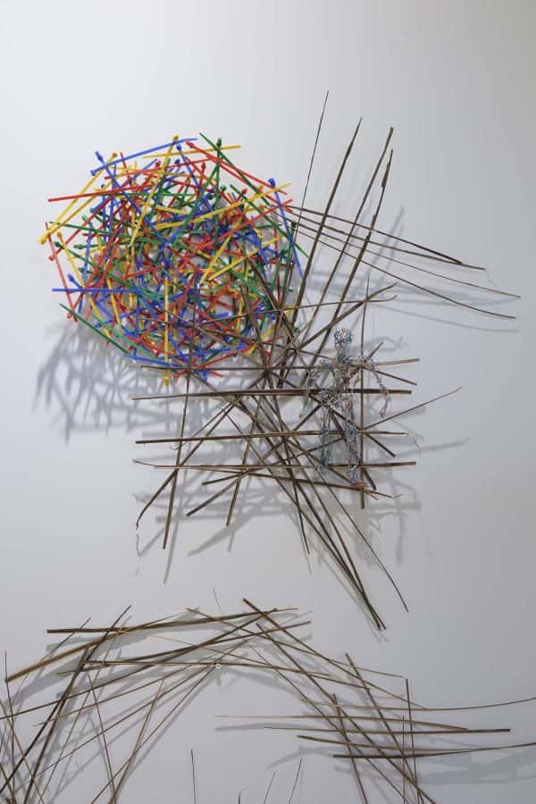 Ian Brownlie - MA Textile Design work showing a multicoloured circle on a white wall made of coloured twigs, surrounded by other natural twigs crossing over each other