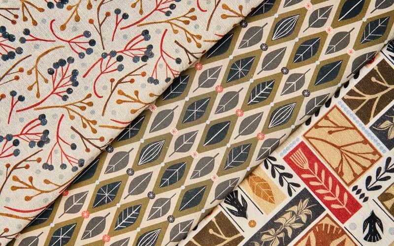 Close up photo of three sets of fabric. On the left, a linear floral pattern in red, blue and brown colour palletes. In the middle, a geometric 70s style leaf print. On the right, block leaf and floral patterns with a variety of colours in a repeat pattern