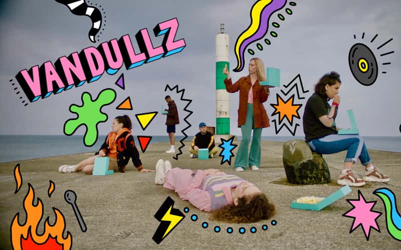 A promotional still for BBC TV series 'Vandullz'. 6 young band members are on a beach pier, some laying, others sitting or standing, surrounded by chips. On the image are graphical geometric pattern illustrations in bright colours, by BA Illustration graduate Ailish Beadle