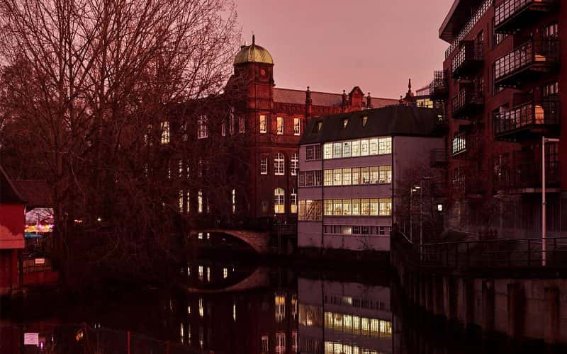 The Norwich University of the Arts St Georges and Guntons buildings shot from across the river under an orange dusk sky