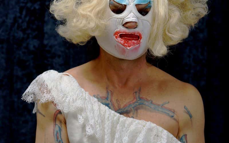 A person dressed up in a dress with tattoos on them, and a wig and a mask.