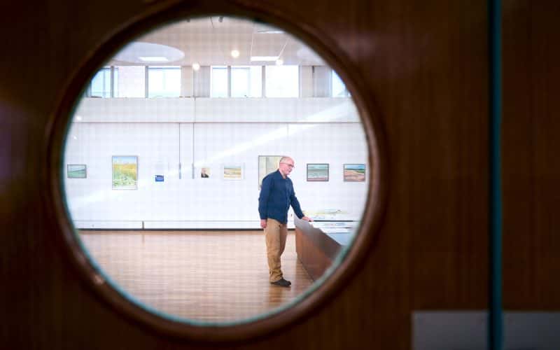 Will Jefferies through a door, looking at paintings, in front of exhibited art work