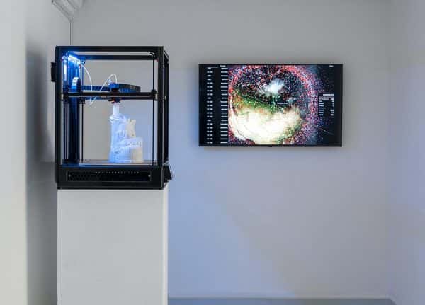 Rematerialiser - A 3D printer on a plinth creates an astronauts boot, in the background a screen shows complex 3D mapping, possible the model being printed