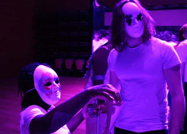  - Figures under purple light wearing eerie masks