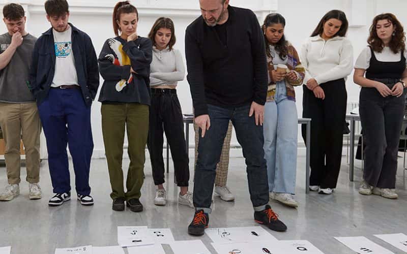 Image showing person leading workshop talking through student work on floor with students in background