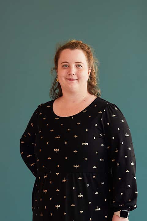 Games Art and Design lecturer Hannah. Hannah wears a black dress with repeating pattern of gold dragonflies and bumble bees