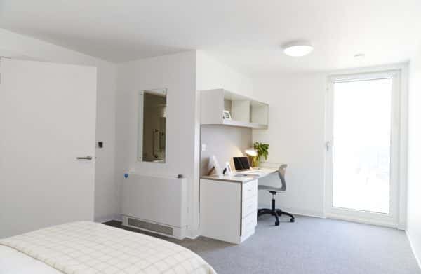 Bedroom - A large, modern bedroom in the All Saints Green accommodation at Norwich University of the Arts. The room has white walls, furniture and ceiling, and a light grey carpet