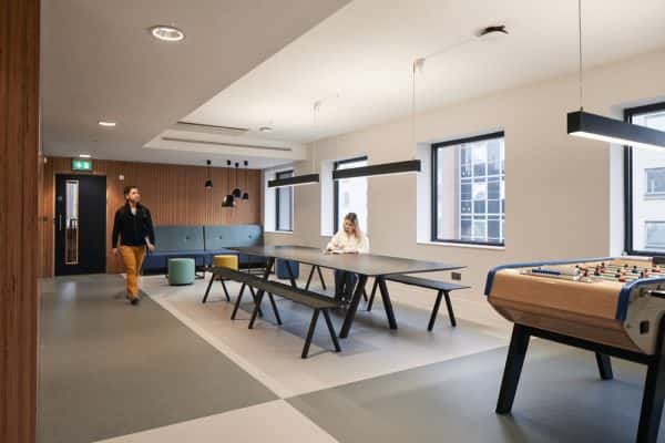 Open plan dining area - Students in a large open plan communal space with long tables, hanging lights, and football table in the Duke Street Riverside accommodation at Norwich University of the Arts