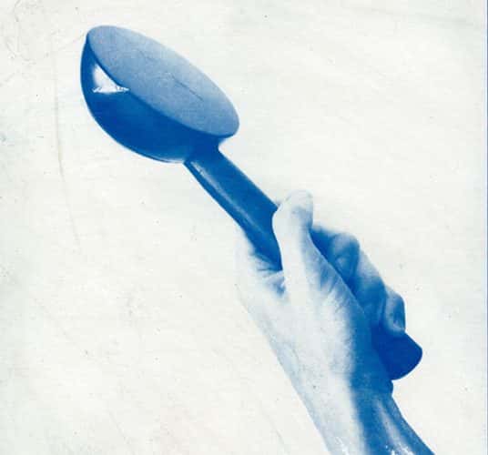  Bold and minimal image in monotone blue wash. The background looks like it could be cyanotype, and the foreground is a hand tightly holding up an object which looks like it could be the end of a watering can, or maybe some kind of measuring spoon. As the arm gets to the end of the page, the detail reduces to blue brushstrokes