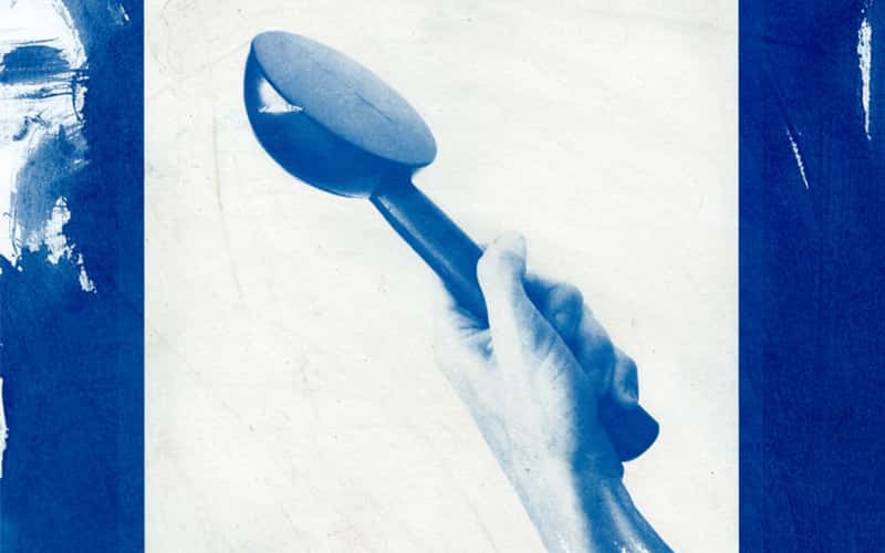 Bold and minimal image in monotone blue wash. The background looks like it could be cyanotype, and the foreground is a hand tightly holding up an object which looks like it could be the end of a watering can, or maybe some kind of measuring spoon. As the arm gets to the end of the page, the detail reduces to blue brushstrokes