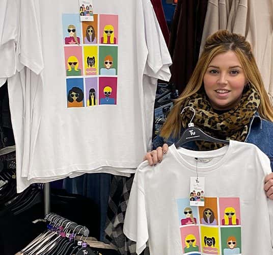  A photo of Evie Thomas in a Sainsbury's store holding a t-shirt with her design on it.